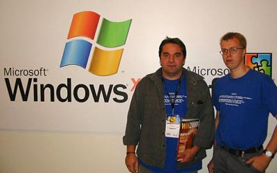 ブルースクリーンのシャツを着てマイクロソフトのロゴの前に立つ人の写真